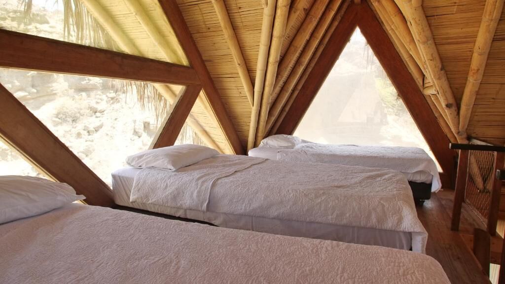 Quarto com duas camas, vigas de madeira e vista para o exterior.