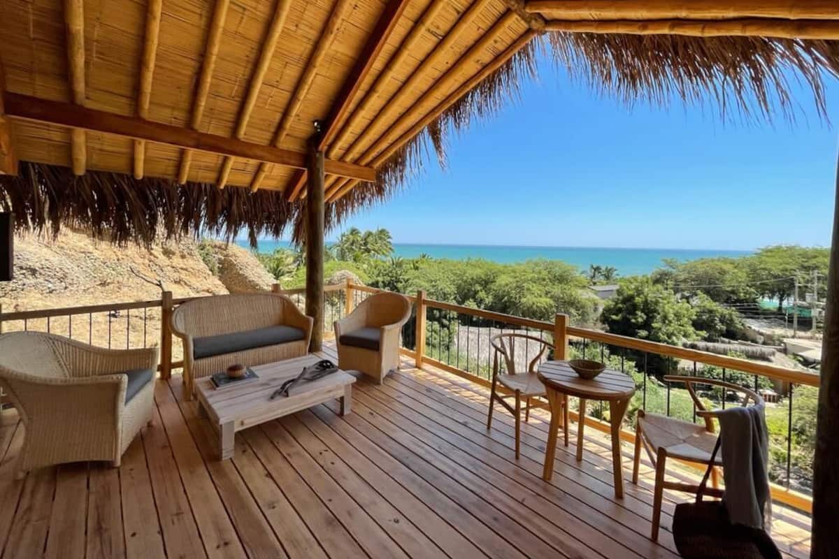 Terraza de madera con muebles de mimbre y techo de paja, con vista a la playa y al océano.
