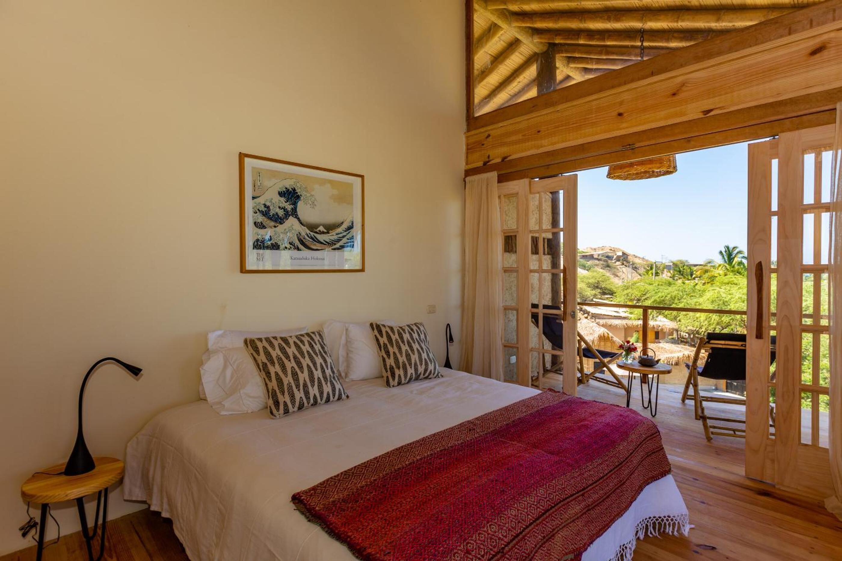 A bedroom with a bed, a painting, a desk, and a balcony with a table and chairs.