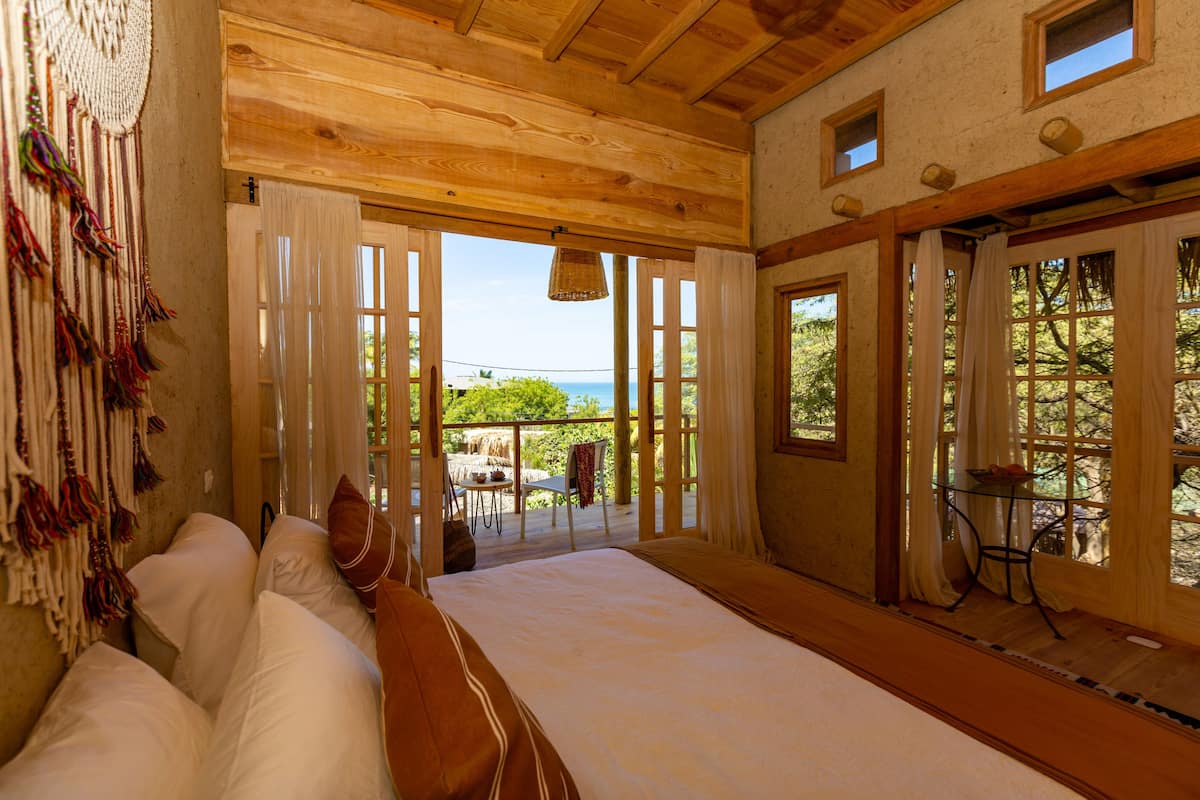 Un dormitorio con una cama grande, techo de madera y vistas al exterior.