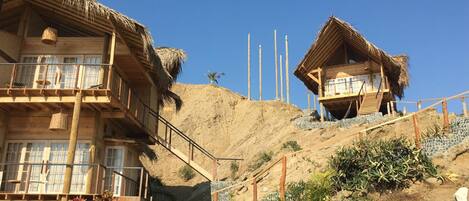 A wooden building with a balcony and a thatched-roof structure on a hillside.