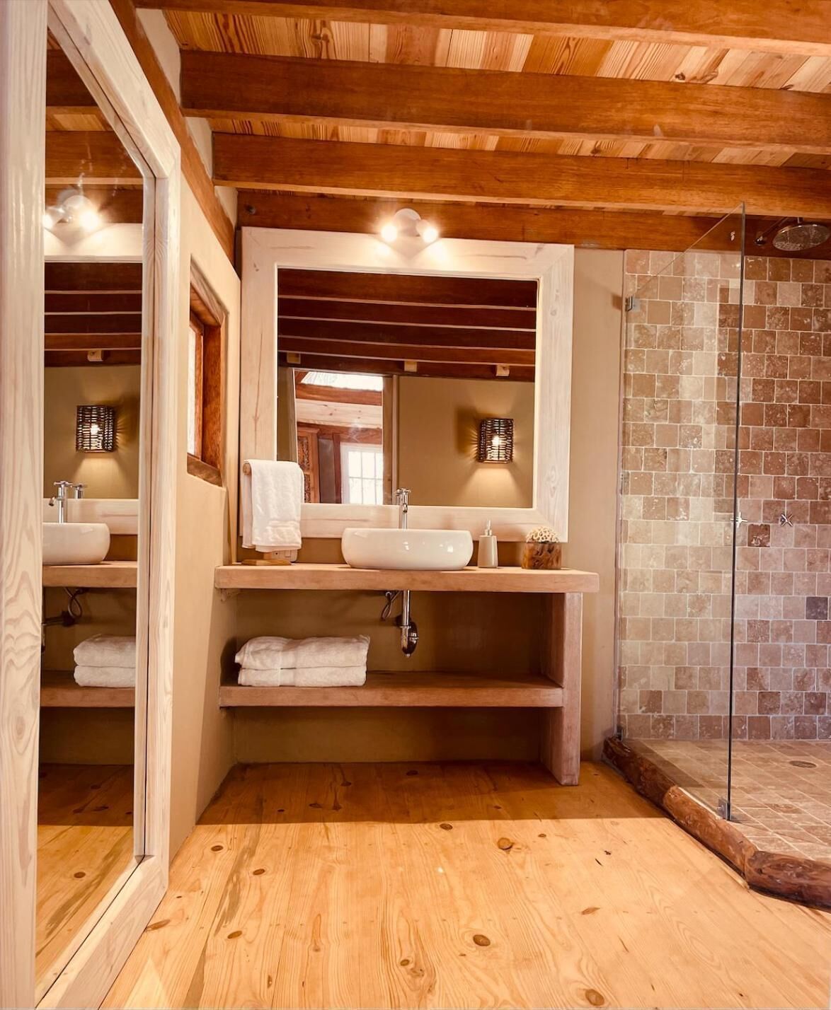Un baño con vigas de madera, dos lavamanos, un espejo y una zona de ducha.