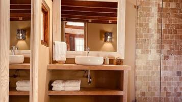 Une salle de bain avec des poutres en bois, deux lavabos, un miroir et un espace douche.