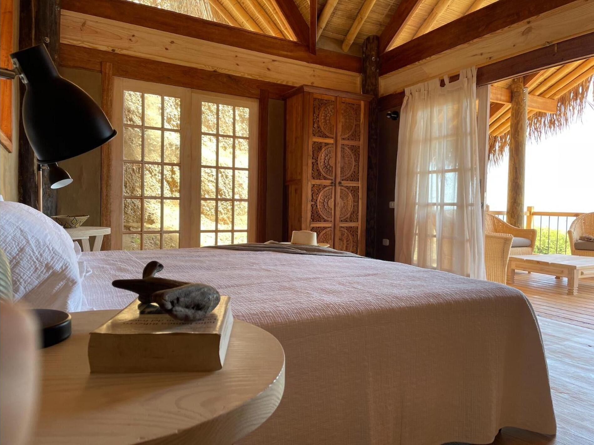 A wooden cabin bedroom with a large bed, a wooden cabinet, and a view of the outdoors.
