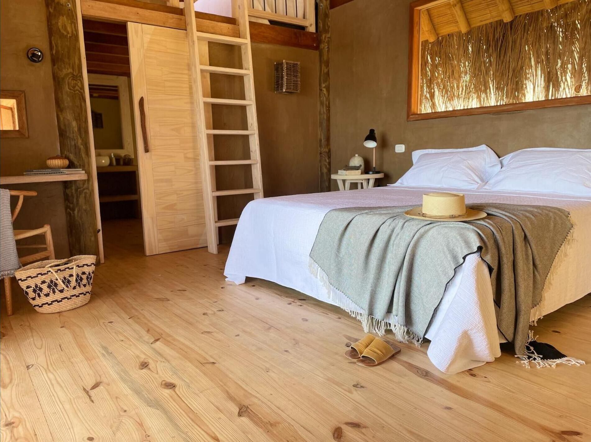 Un dormitorio con suelo de madera, una cama, una escalera, un escritorio y una mesita.
