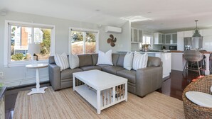 A modern living room with a sectional sofa, a white coffee table, and a wicker chair. - Beautiful Hen Cove - Book Your 2026 Trip (Pocasset, Bourne)