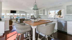 A spacious kitchen with a wooden island, wicker chairs, and a view of the ocean. - Beautiful Hen Cove - Book Your 2026 Trip (Pocasset, Bourne)