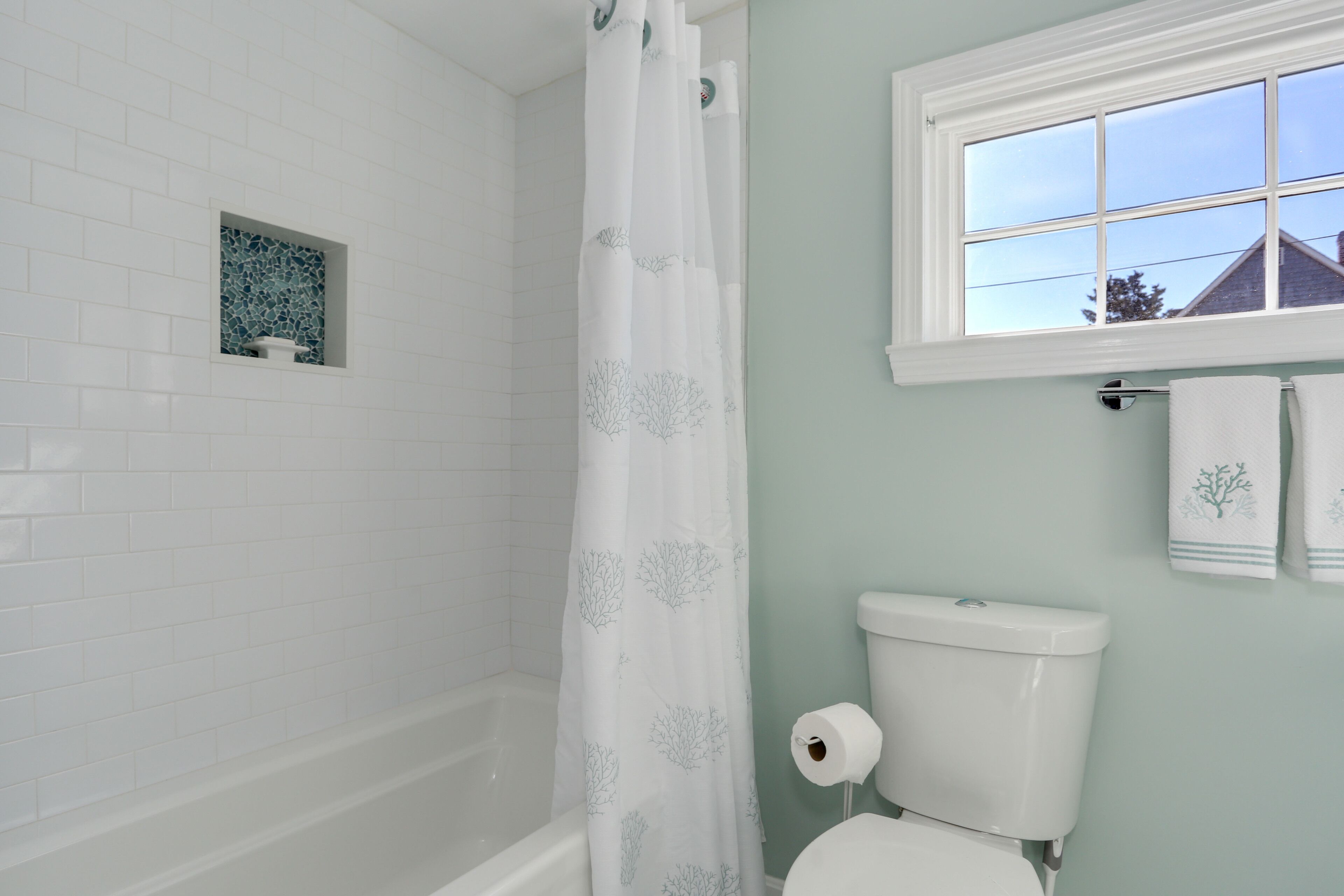 A bathroom with a white bathtub, a toilet, and a shower curtain with a leaf pattern.