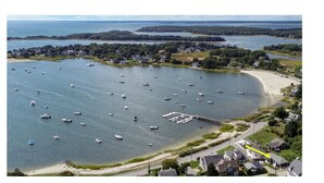 An aerial view of a coastal area with a marina, boats, and residential buildings. - Beautiful Hen Cove - Book Your 2026 Trip (Pocasset, Bourne)