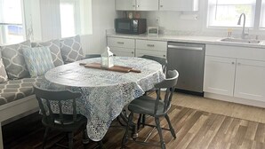 Una cocina moderna con armarios blancos, un microondas y un lavabo. Hay una zona de comedor con una mesa redonda y sillas, y un sofá con cojines estampados.