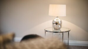A round glass table with a metallic base and a white lampshade. - Waterfront Apartments (Douglas)