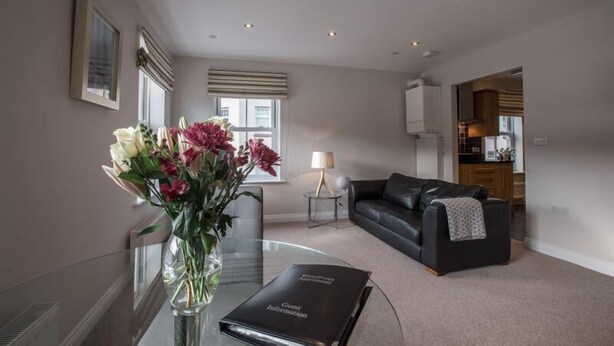 A modern living room with a glass coffee table, a black leather sofa, and a vase of flowers. - Waterfront Apartments (Douglas)