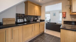 A modern kitchen with wooden cabinets, black countertops, and a black tiled backsplash. - Waterfront Apartments (Douglas)