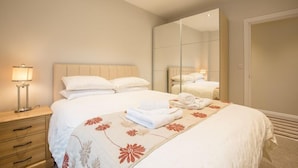 A hotel bedroom with a bed, a nightstand, a mirror, and a wardrobe. - Waterfront Apartments (Douglas)