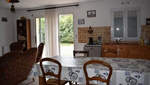 Zona pranzo con tavolo imbandito per quattro persone, sedie in legno, una libreria e angolo cottura con lavello e fornelli.