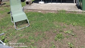 Un'area patio con una zona salotto coperta, una sedia a sdraio e un cestino verde.