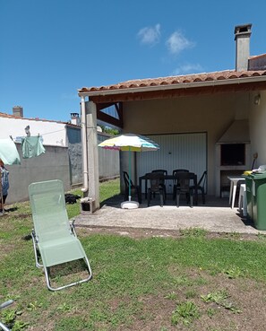 Ein Patio mit überdachter Sitzecke, einem Liegestuhl und einer grünen Mülltonne.