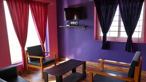 Habitació amb parets morades, un televisor de pantalla plana muntat a una estant i una taula de fusta amb quatre cadires.