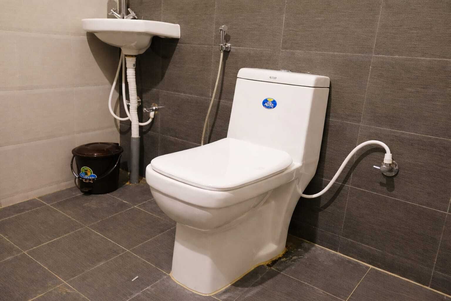Un bagno con un water bianco, un lavandino e un secchio nero.