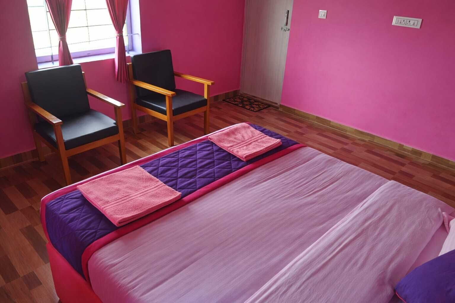 Een kamer met een bed, twee stoelen en een raam met gordijnen.