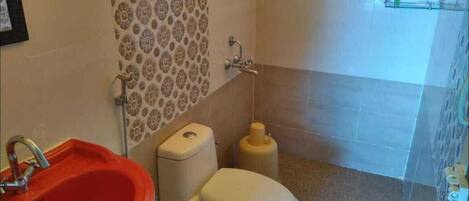 A bathroom with a red sink, a white toilet, patterned wall tiles, and a shower area.