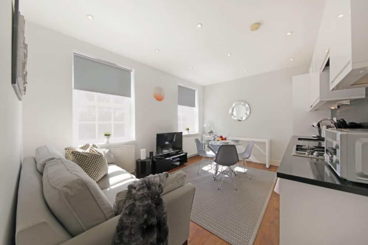 A modern living room with a sofa, a TV, and a dining area with a table and chairs.
