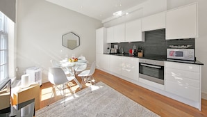 A modern kitchen with white cabinets, a microwave, and a dining area with a glass table and chairs. -  Executive Apartments in Central London Euston FREE WiFi by City Stay Aparts (London)