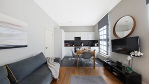 A modern living room with a grey sofa, a dining table with chairs, a flat-screen TV, and a kitchen in the background. -  Executive Apartments in Central London Euston FREE WiFi by City Stay Aparts (London)