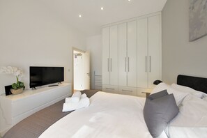 A modern hotel room with a large bed, a TV on a white console, a wardrobe, and a potted plant.