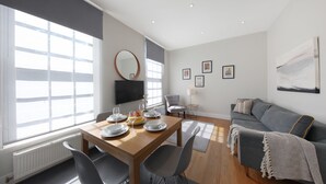 A modern living room with a dining table set for four, a grey sofa, and a large window providing natural light. -  Executive Apartments in Central London Euston FREE WiFi by City Stay Aparts (London)