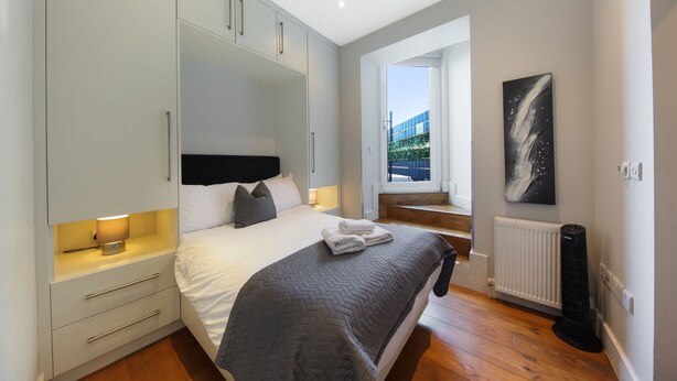 A bedroom with a bed, bedside table, wardrobe, radiator, and a window with a view. -  Executive Apartments in Central London Euston FREE WiFi by City Stay Aparts (London)