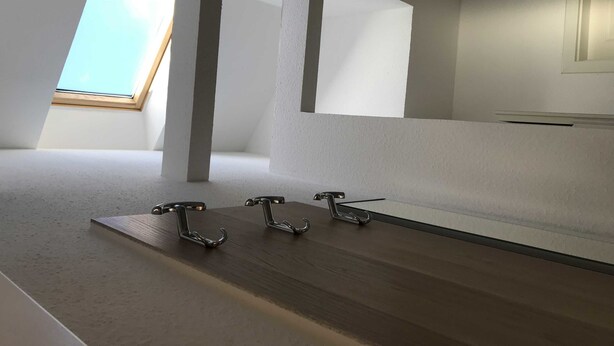 Una habitación moderna y minimalista con techo inclinado, tragaluz y tres ganchos metálicos en el suelo.