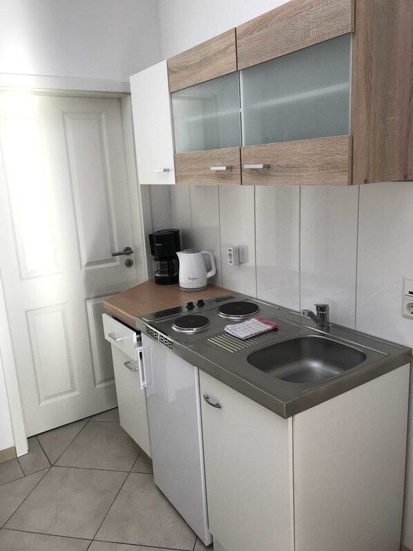 A compact kitchen with a built-in stove, a sink, and wooden cabinets. - Wohnen am Wanderweg (Aurich)