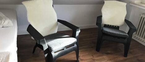 Two black chairs with white fur throws in a room with wooden flooring and white walls.