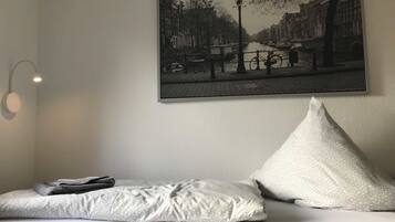A bed with a pillow and a blanket, a wall-mounted picture of a canal, and a wall-mounted light fixture.