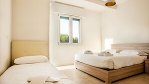 A bedroom with two beds, a window with a view, and a hanging light fixture. - Condominio Villa Mauro (Jesolo)