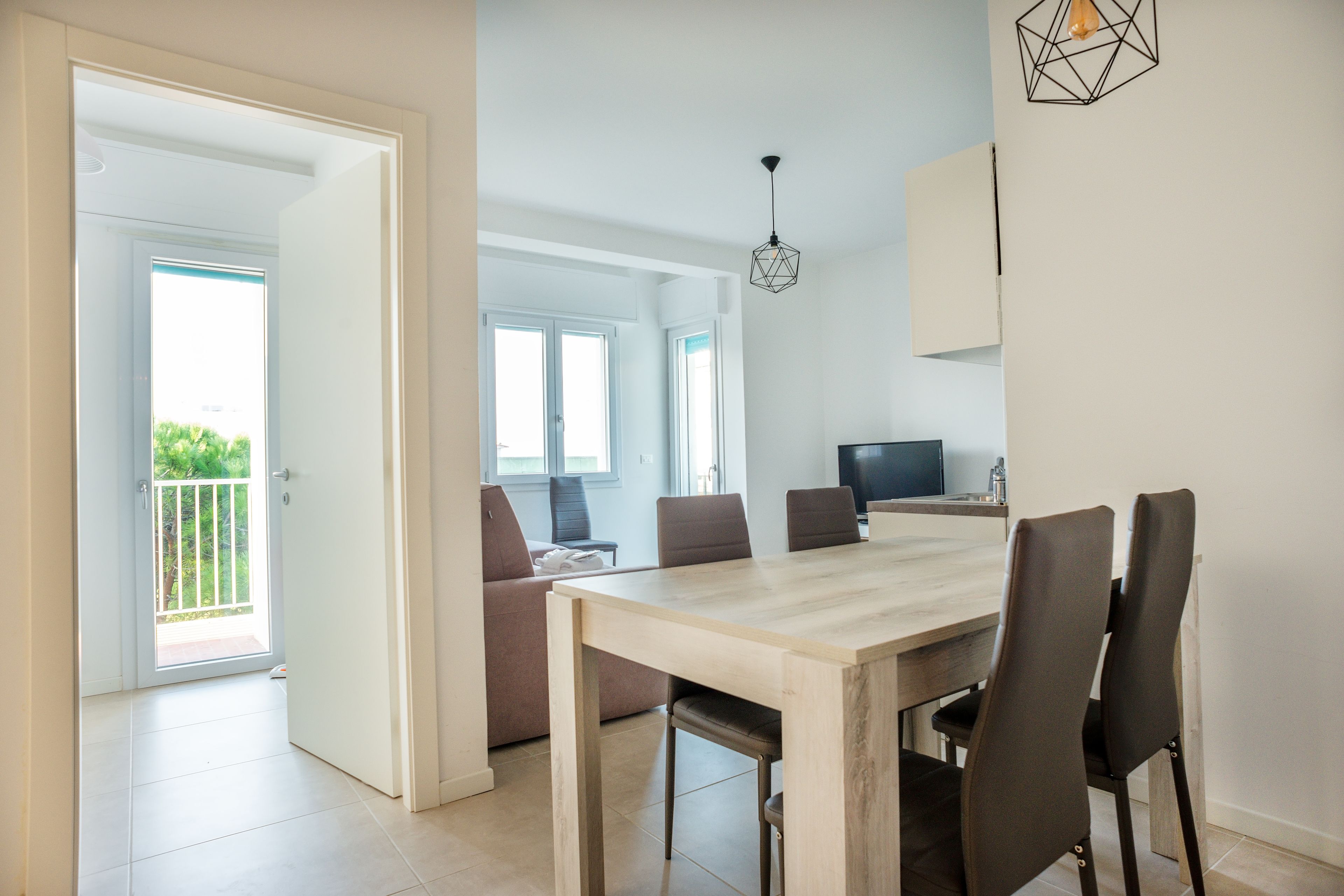 Un comedor con una mesa y sillas de madera, un televisor sobre un mueble bajo, y un balcón con vistas.