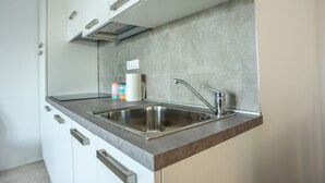 A modern kitchen with stainless steel appliances, a double sink, and a grey tiled backsplash. - Condominio Villa Mauro (Jesolo)