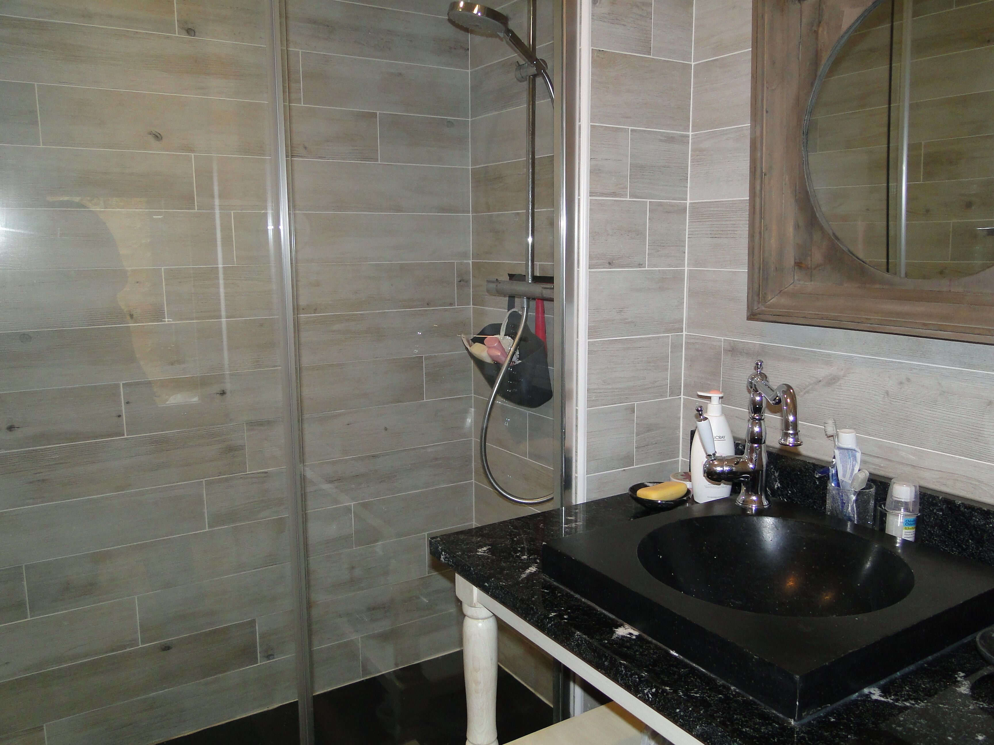 Un baño con lavamanos negro, un espejo y una ducha con puerta de cristal.