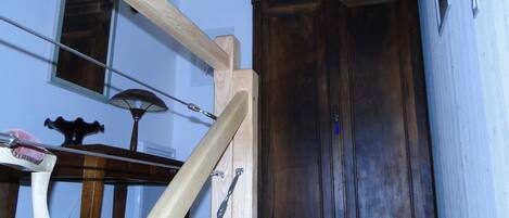 A room with a wooden staircase, a large wooden wardrobe, and a small table with a lamp.