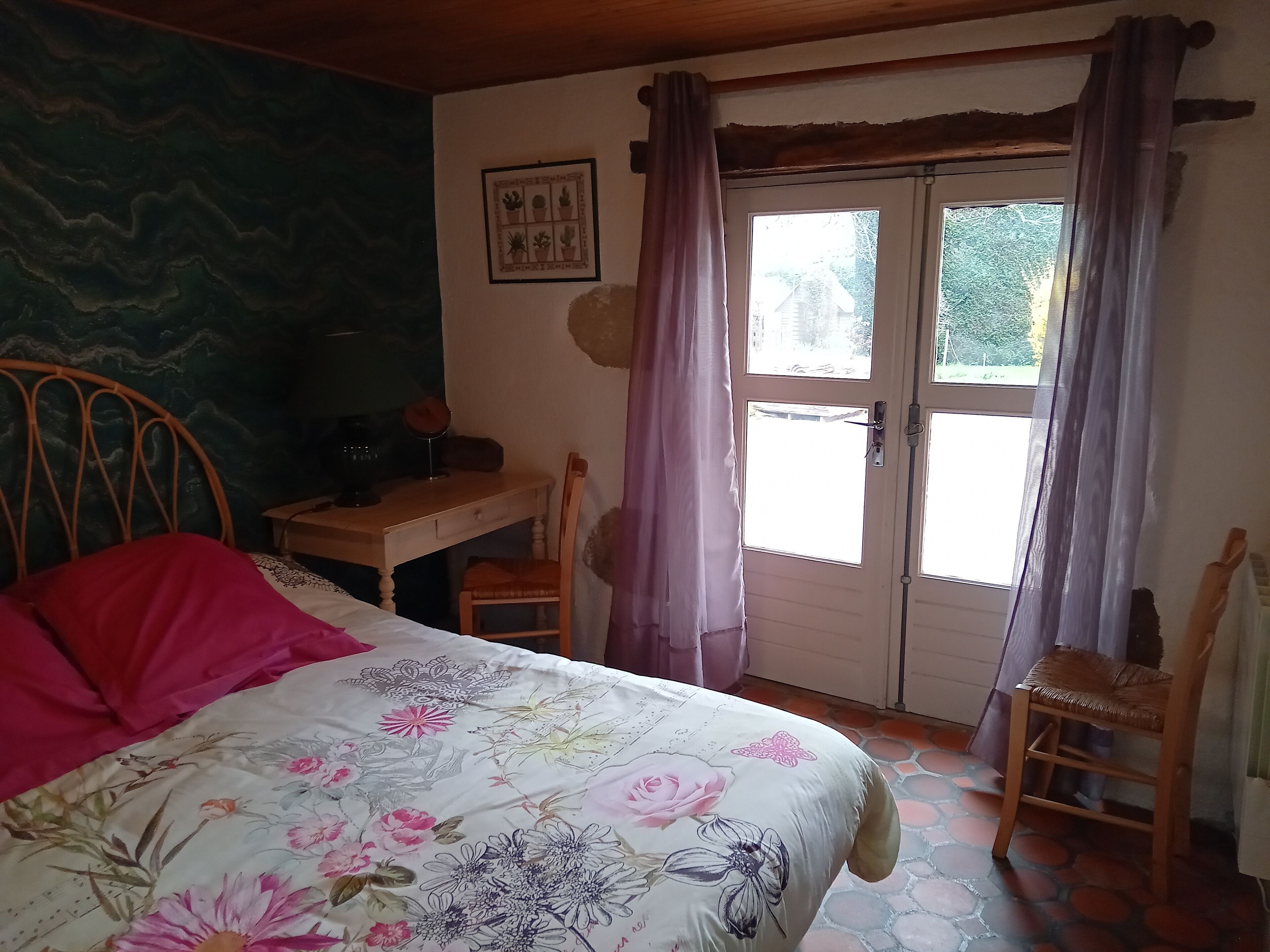Ein Schlafzimmer mit Bett, Schreibtisch und Stuhl. Ein Fenster mit Vorhängen und eine Tür sind vorhanden.
