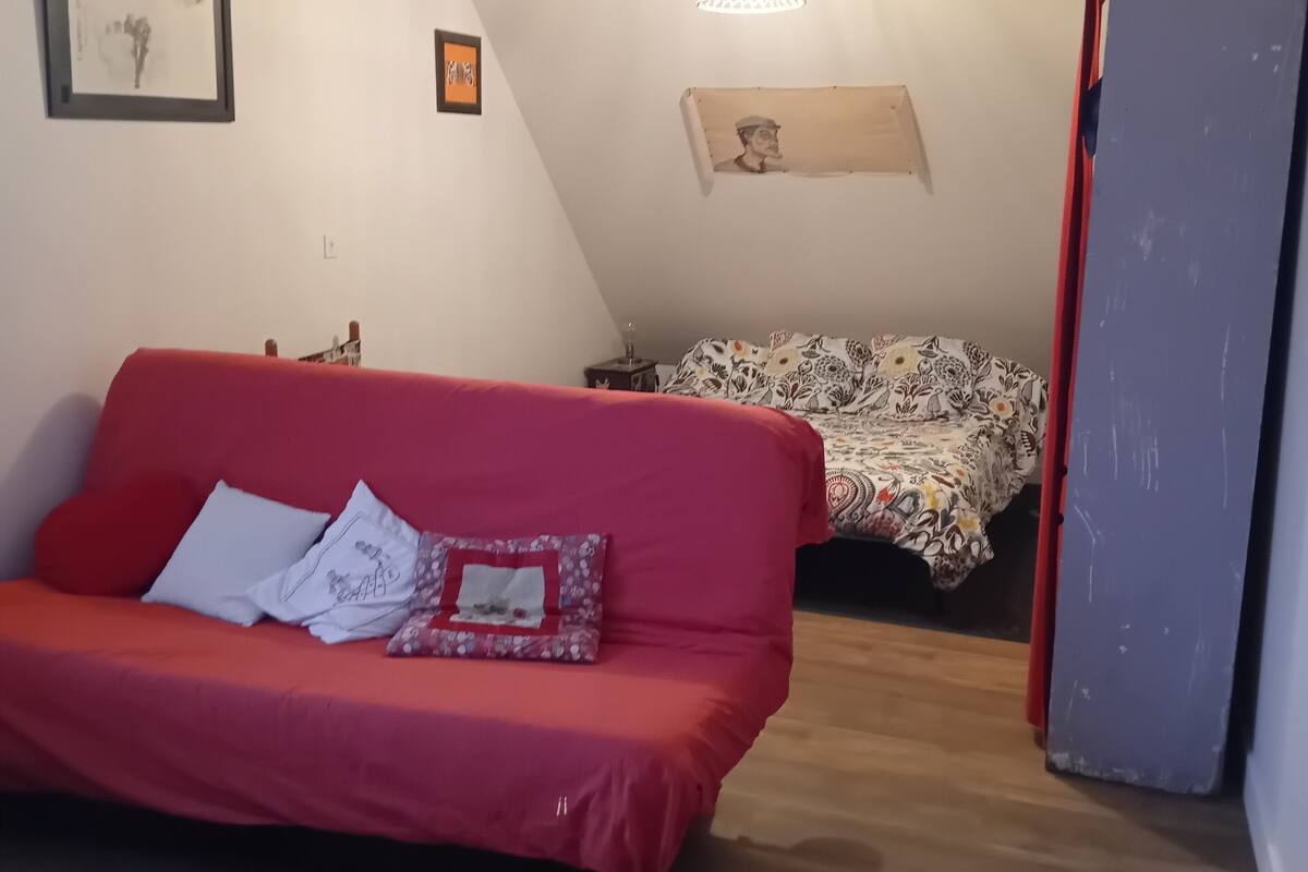 A small, cozy room with a red sofa, a patterned bed, and a ceiling fan.