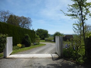 A gravel driveway leading to a gated entrance surrounded by lush greenery and a clear sky. - La Maison de Barbara (Effiat)