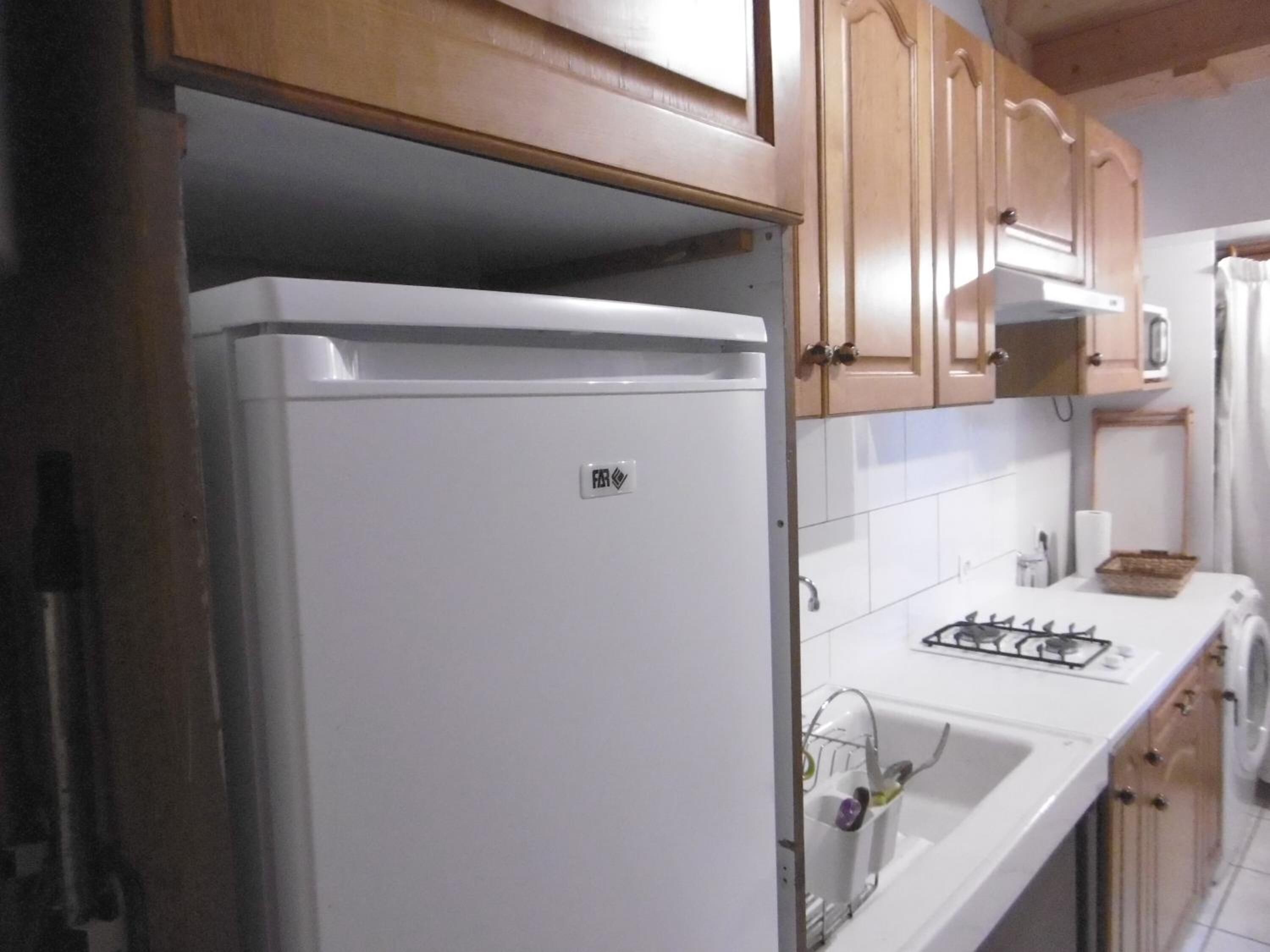 Une cuisine avec des meubles de rangement en bois, un réfrigérateur blanc, une cuisinière à gaz et un lave-linge.
