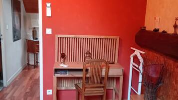 A room with a red wall, wooden desk, chair, and a bed with a colorful quilt.