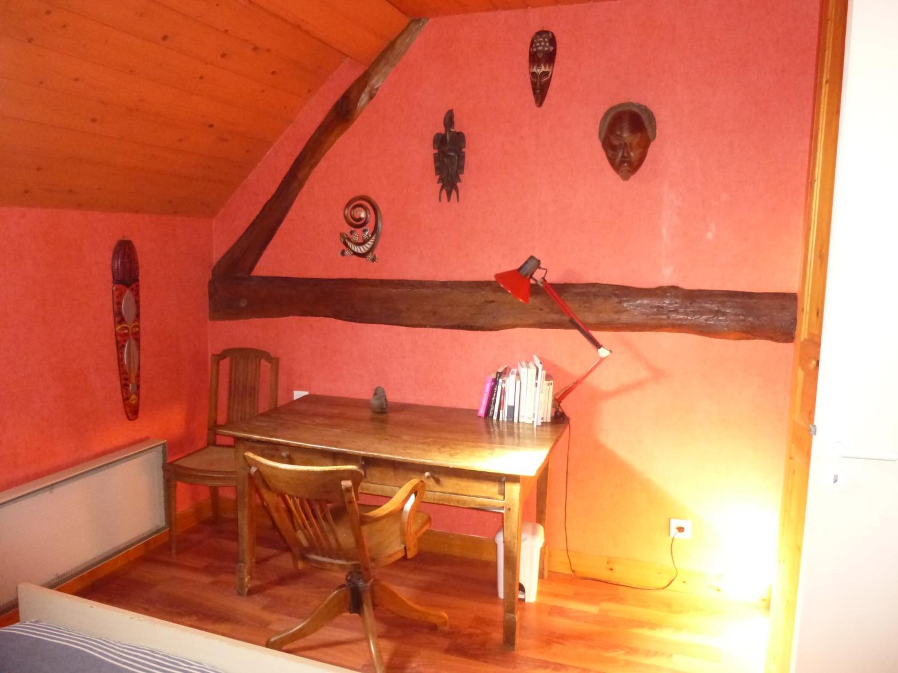 Un área de comedor con una mesa y sillas de madera, una pared roja con máscaras decorativas y una lámpara de escritorio roja.