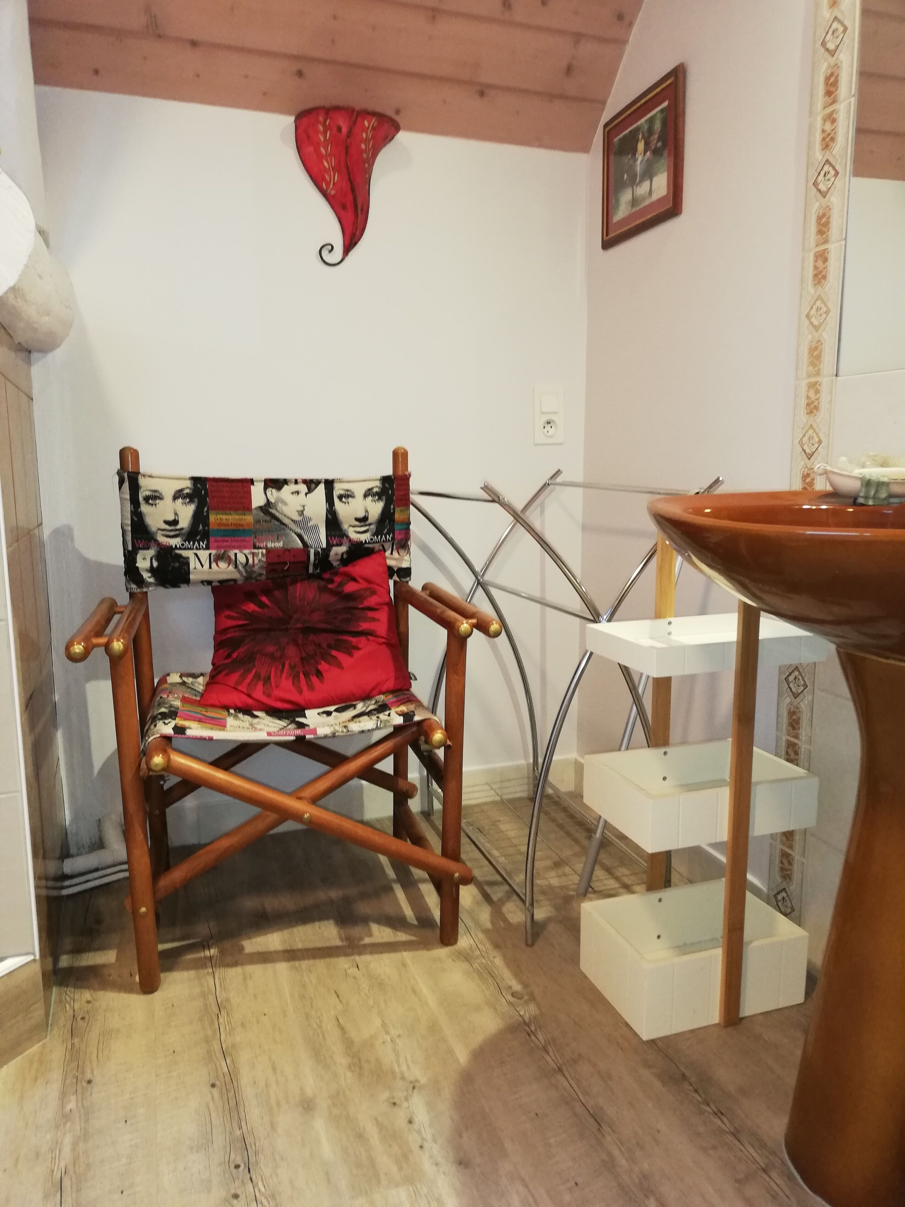 Una sedia in legno con lo schienale rivestito da una copertina di rivista, un cuscino rosso e una scala in metallo.
