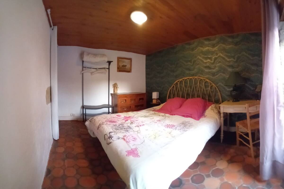 A bedroom with a bed, a desk, a chair, a dresser, and a wall with a wavy pattern.