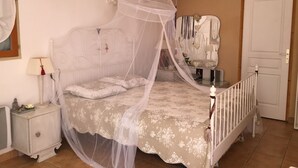 Ein Schlafzimmer mit Himmelbett, Nachttisch, Spiegel und einer Tür.