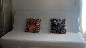 Ein weißes Sofa mit zwei Zierkissen, ein Gemälde darüber und ein Fenster zur rechten Seite.